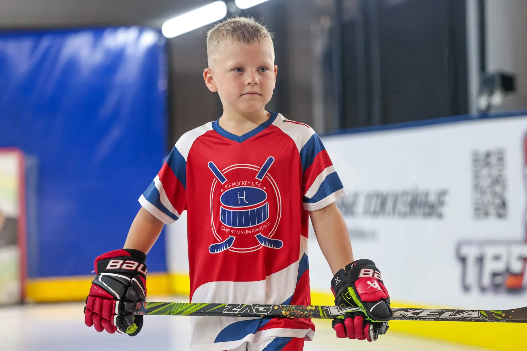 Мальчик в красной форме Ice Hockey Life с клюшкой
